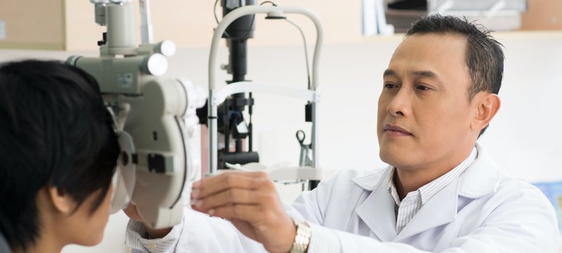 Young male Asian doctor performing an eye exam.